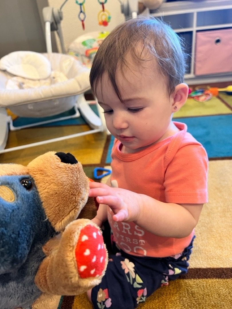 An infant exploring a soft stuffed animal on the classroom rug