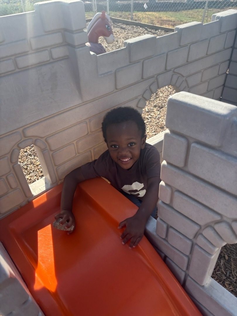 A smiling child at the top of the playground slide